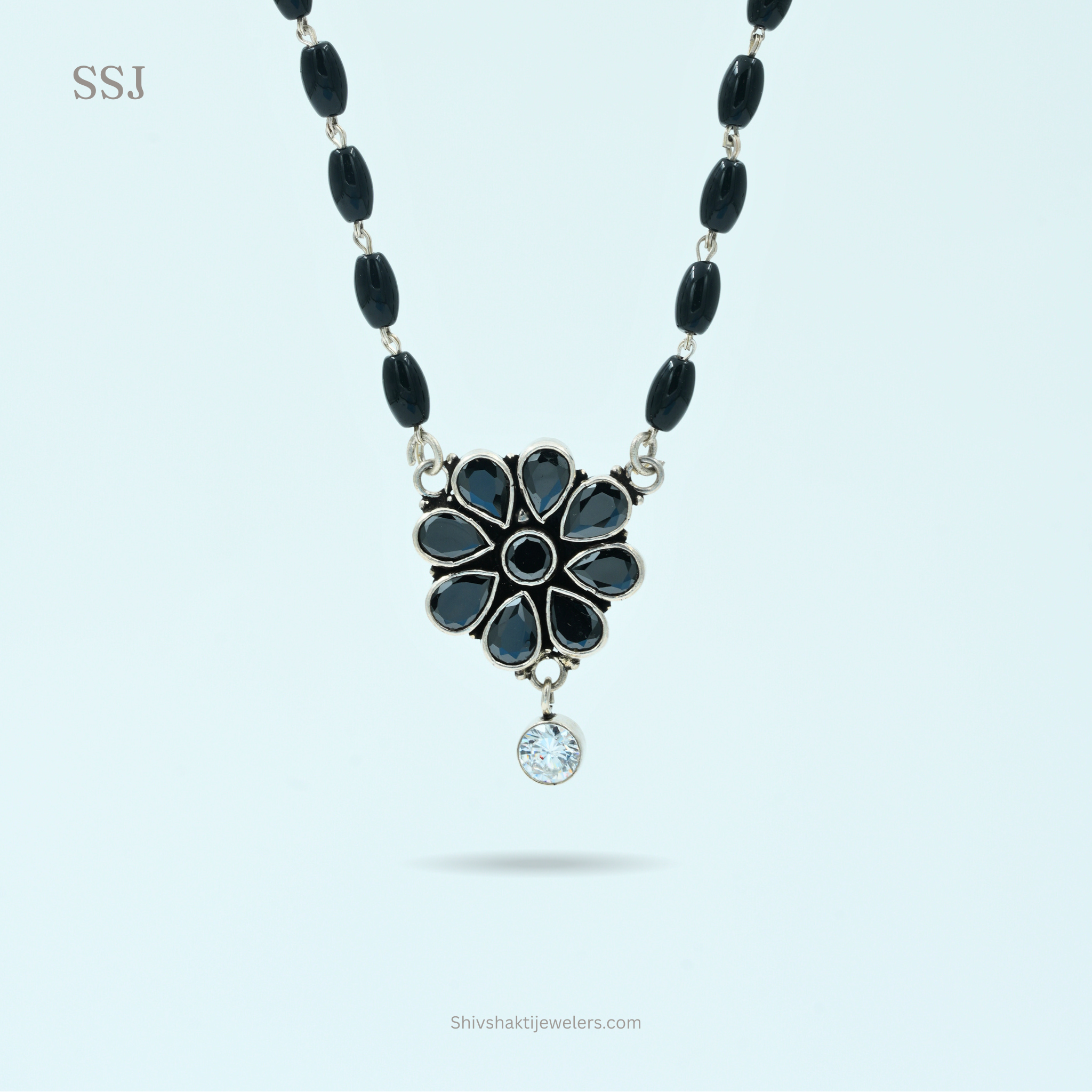 Necklace with black beads and a floral pendant on a light blue background