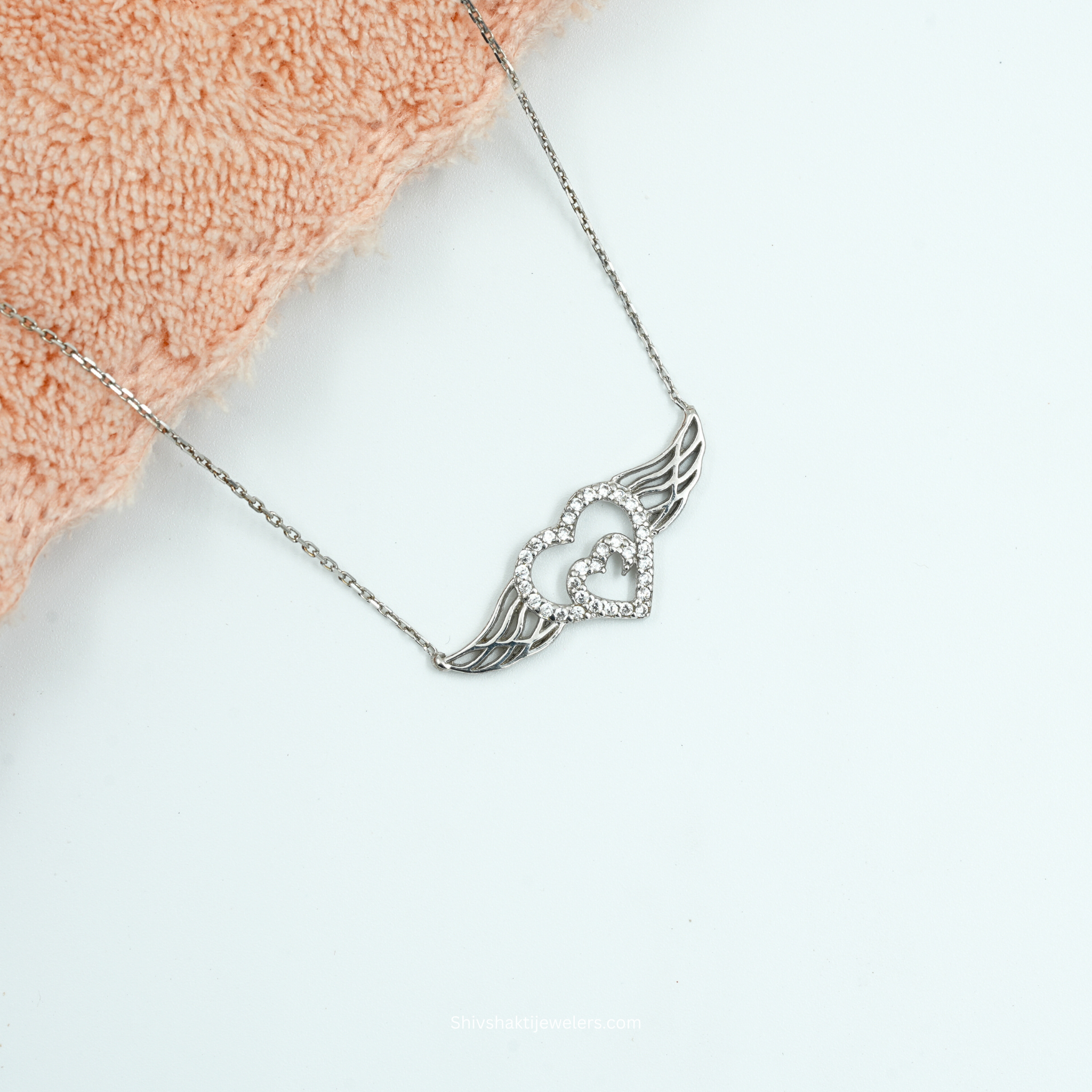 Silver necklace with a heart and wing design on a light background