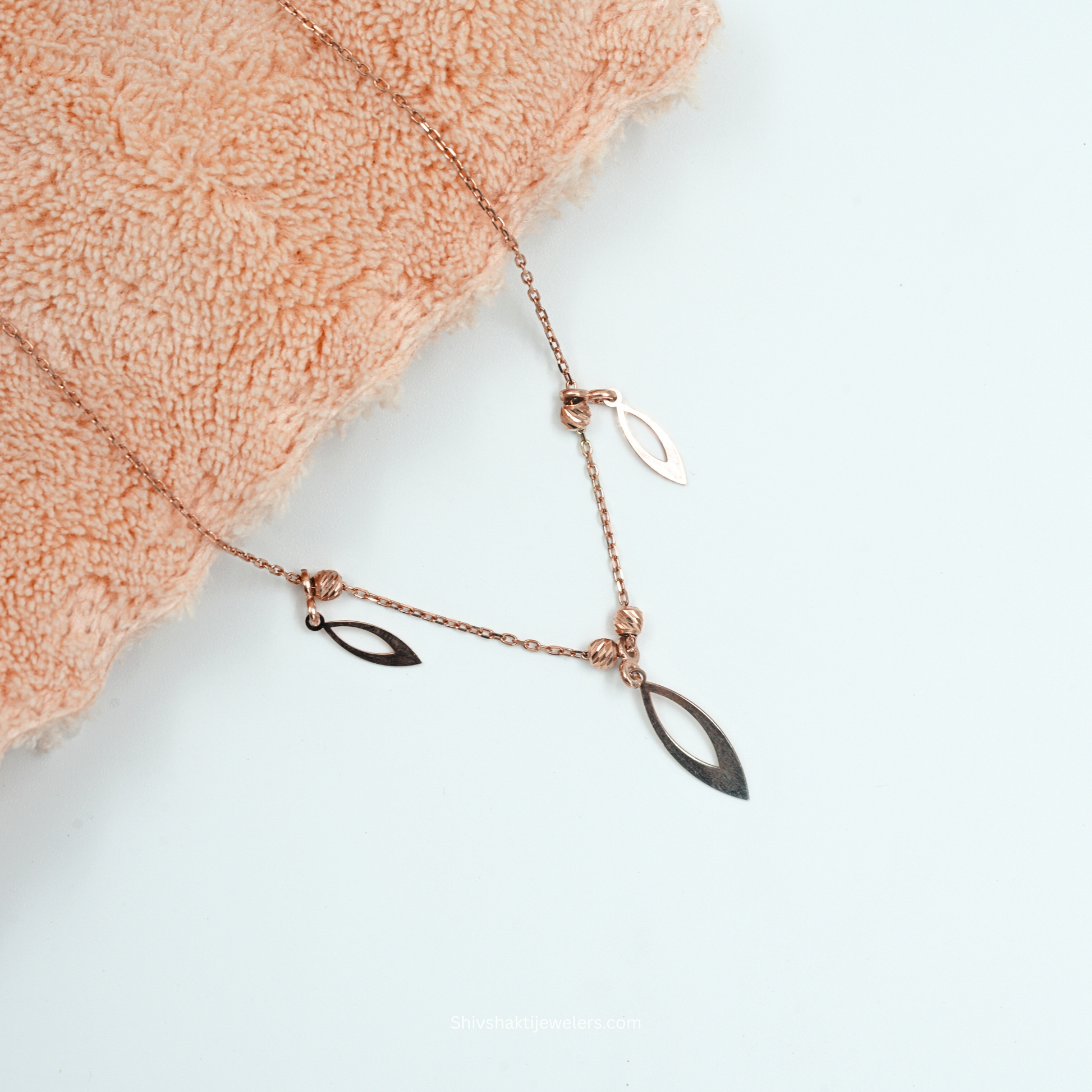 Rose gold necklace with leaf-shaped pendants on a light background
