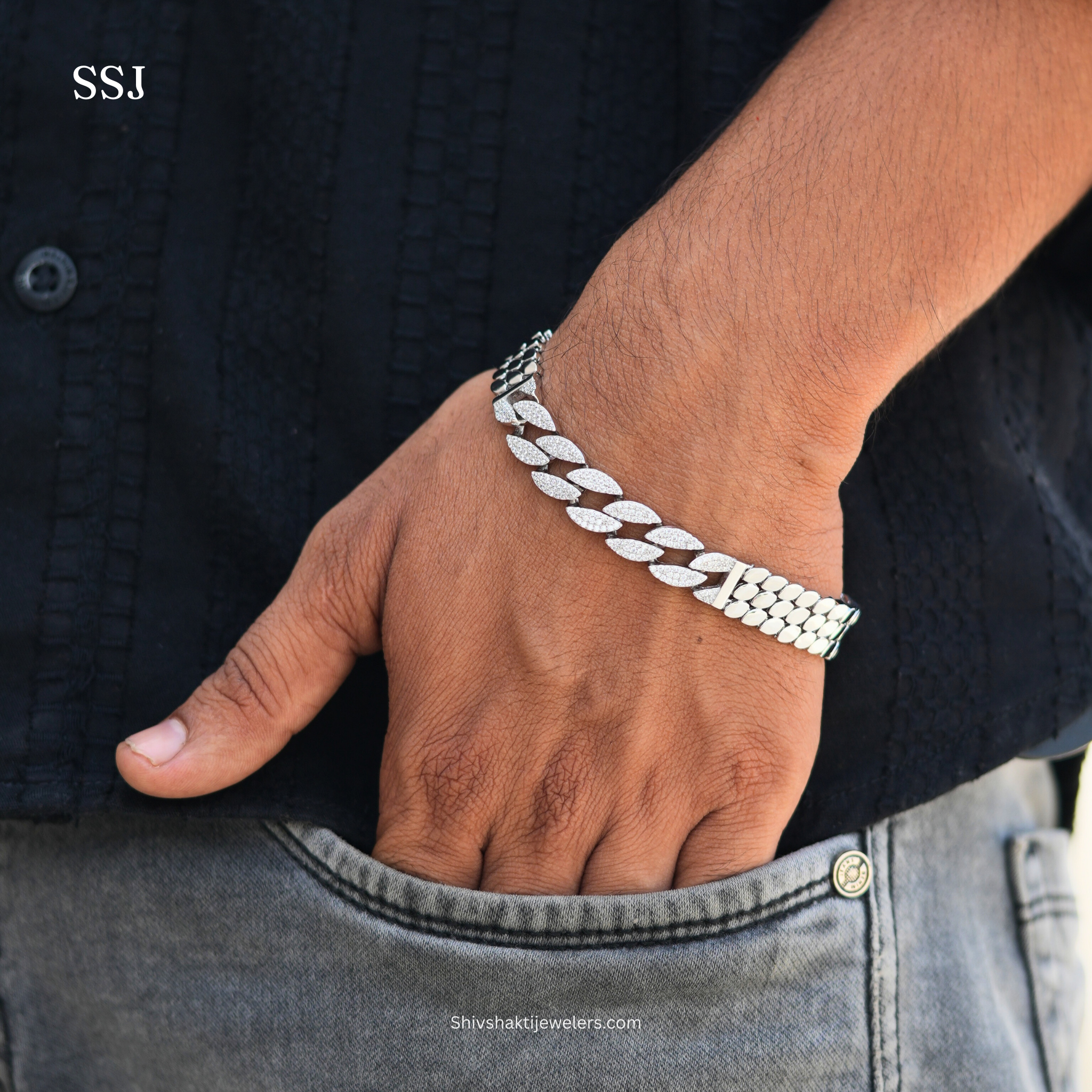 Silver chain bracelet on a wrist with a dark shirt and jeans background