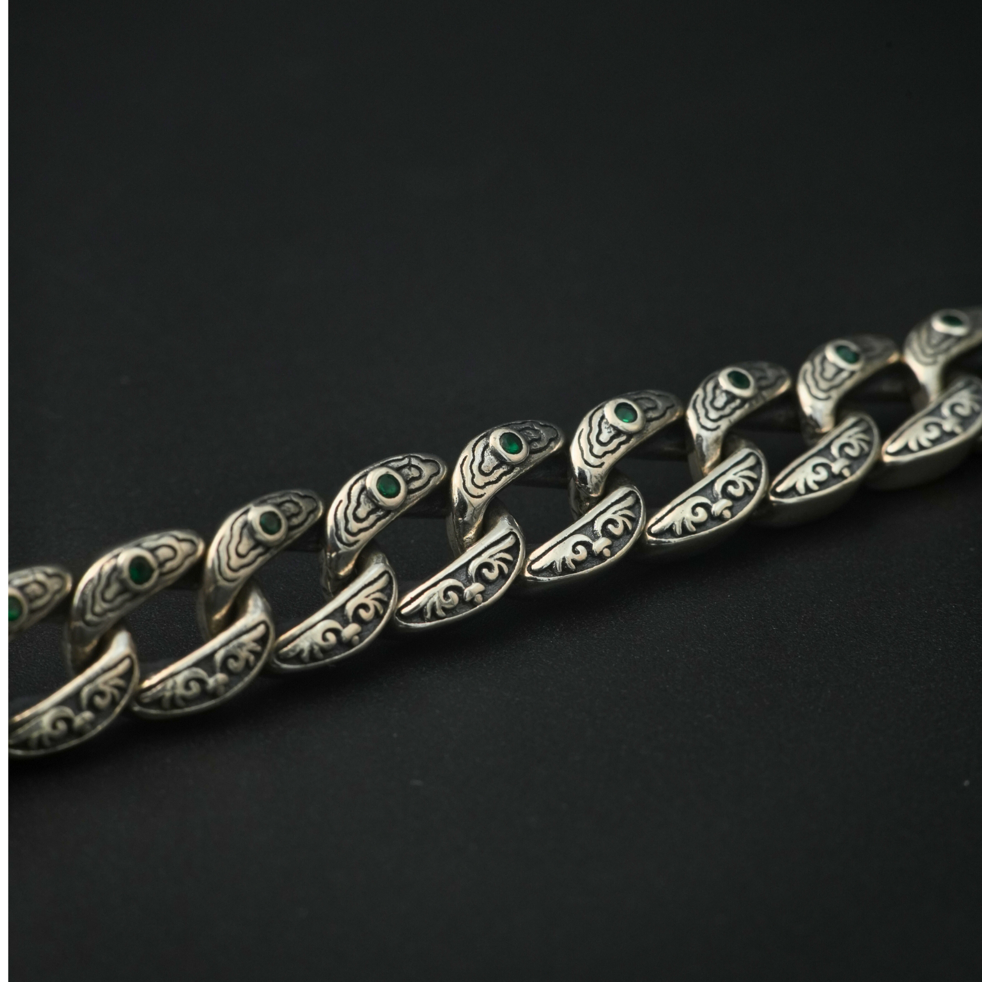 Close-up of tribal engraved curb chain links with emerald accents