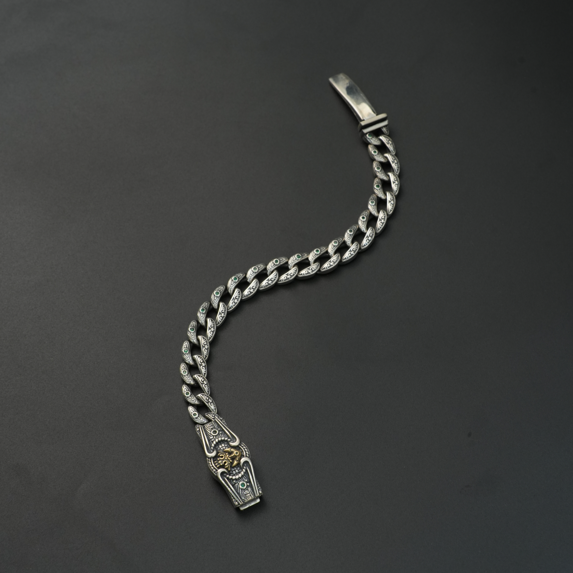 Oxidized silver lion head bracelet with emerald stone inlays on black background