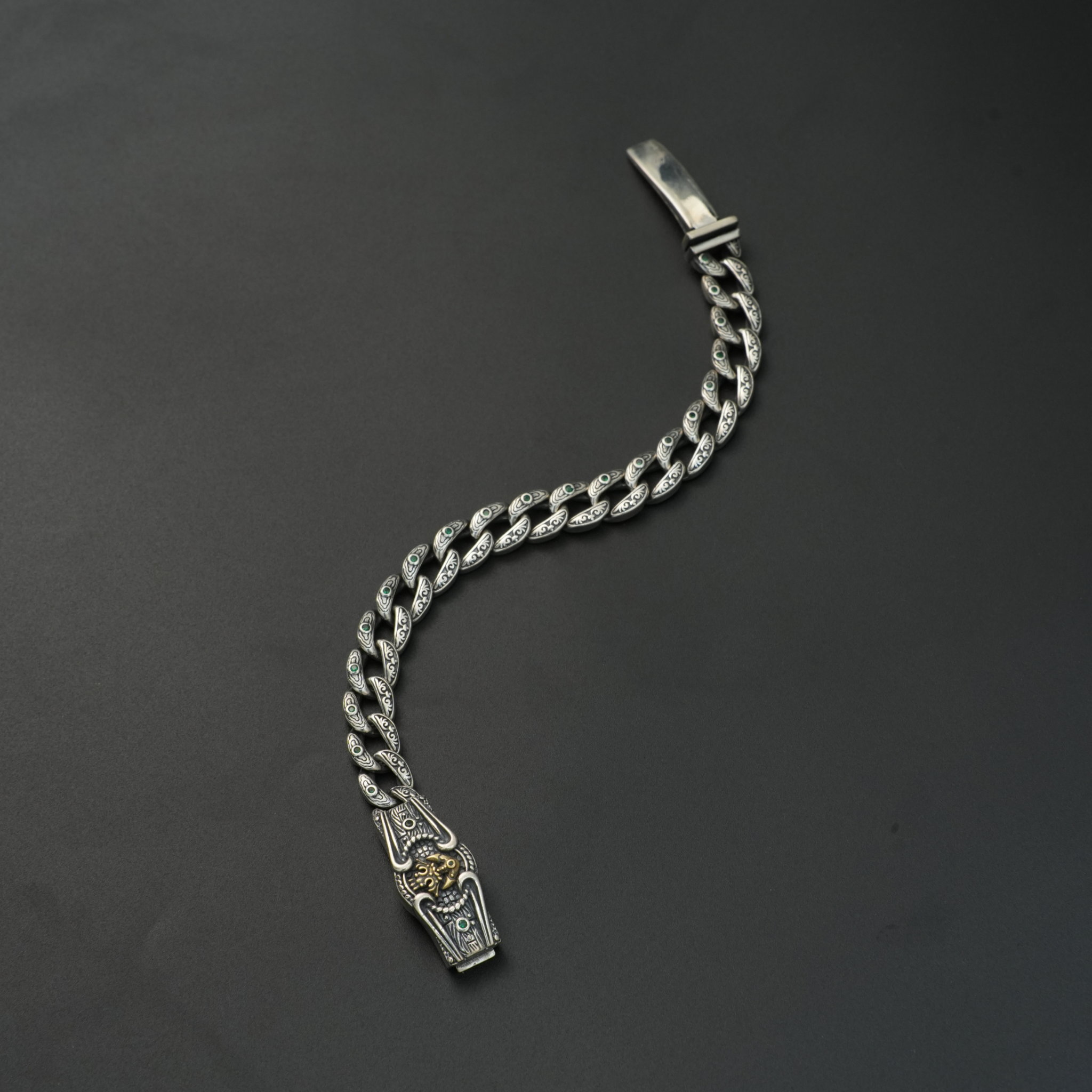 Oxidized silver lion head bracelet with emerald stone inlays on black background