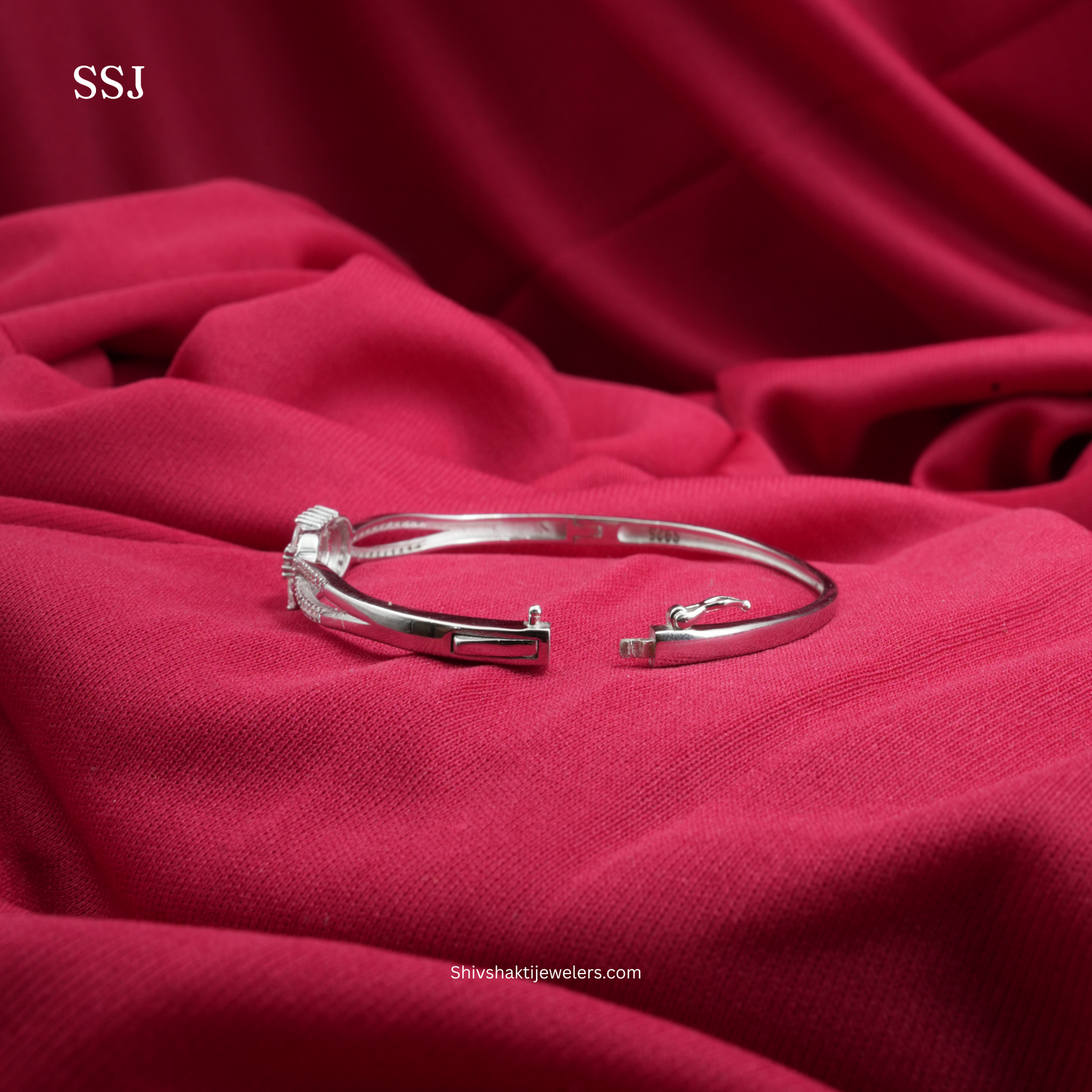 Silver bracelet on a red fabric background with 'SSJ' branding.