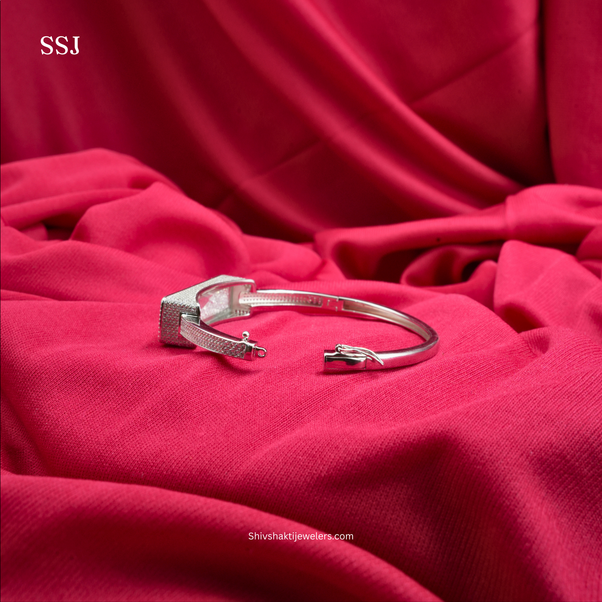 Silver bracelet on a red fabric background with 'SSJ' branding.