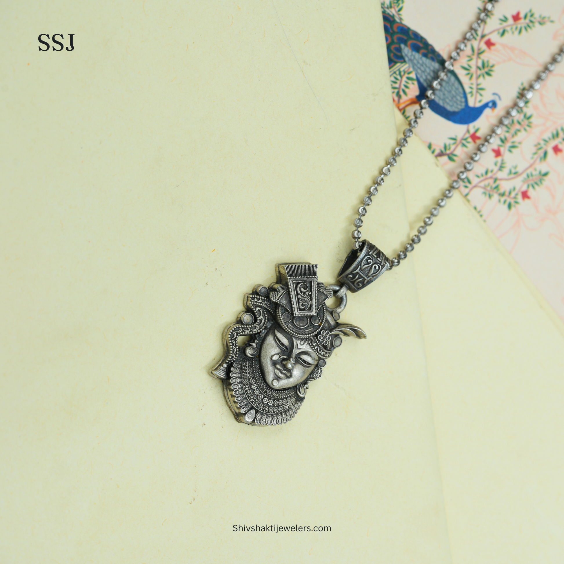 Silver pendant necklace on a light green background with 'SSJ' branding.