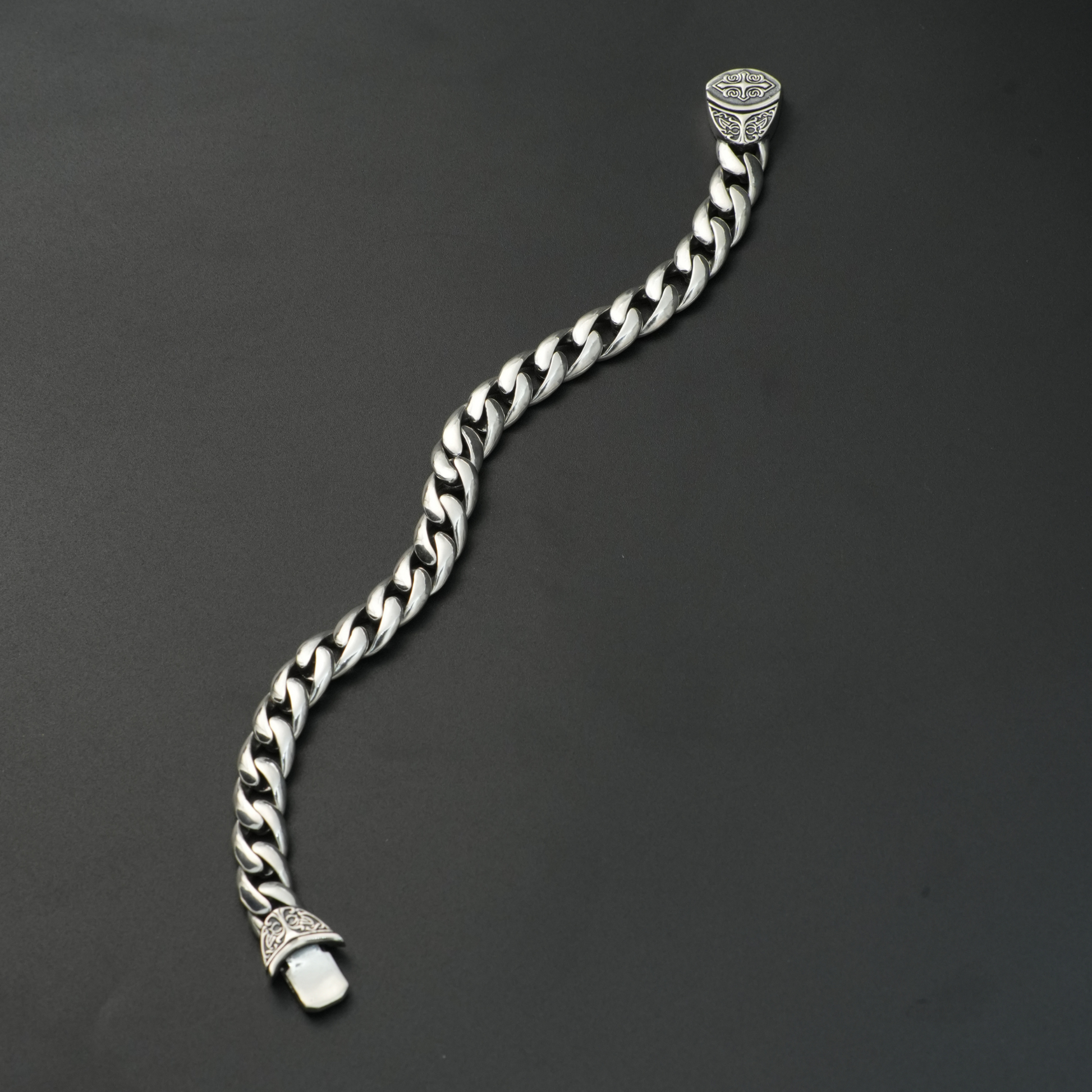 Heavy silver curb chain bracelet with engraved end caps on black background