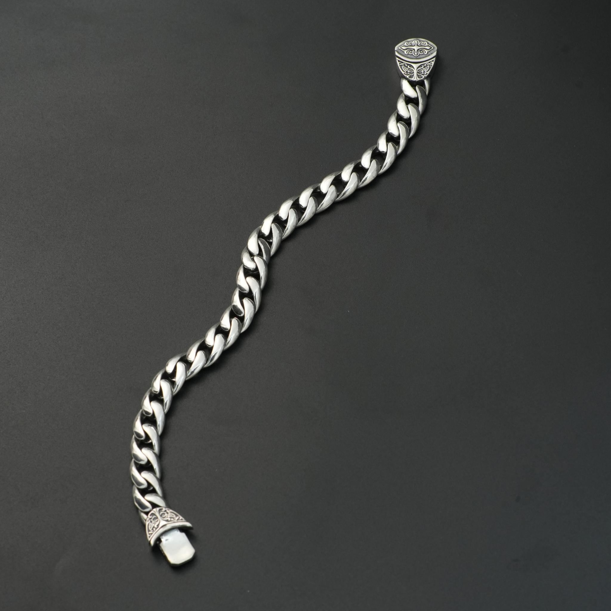 Heavy silver curb chain bracelet with engraved end caps on black background