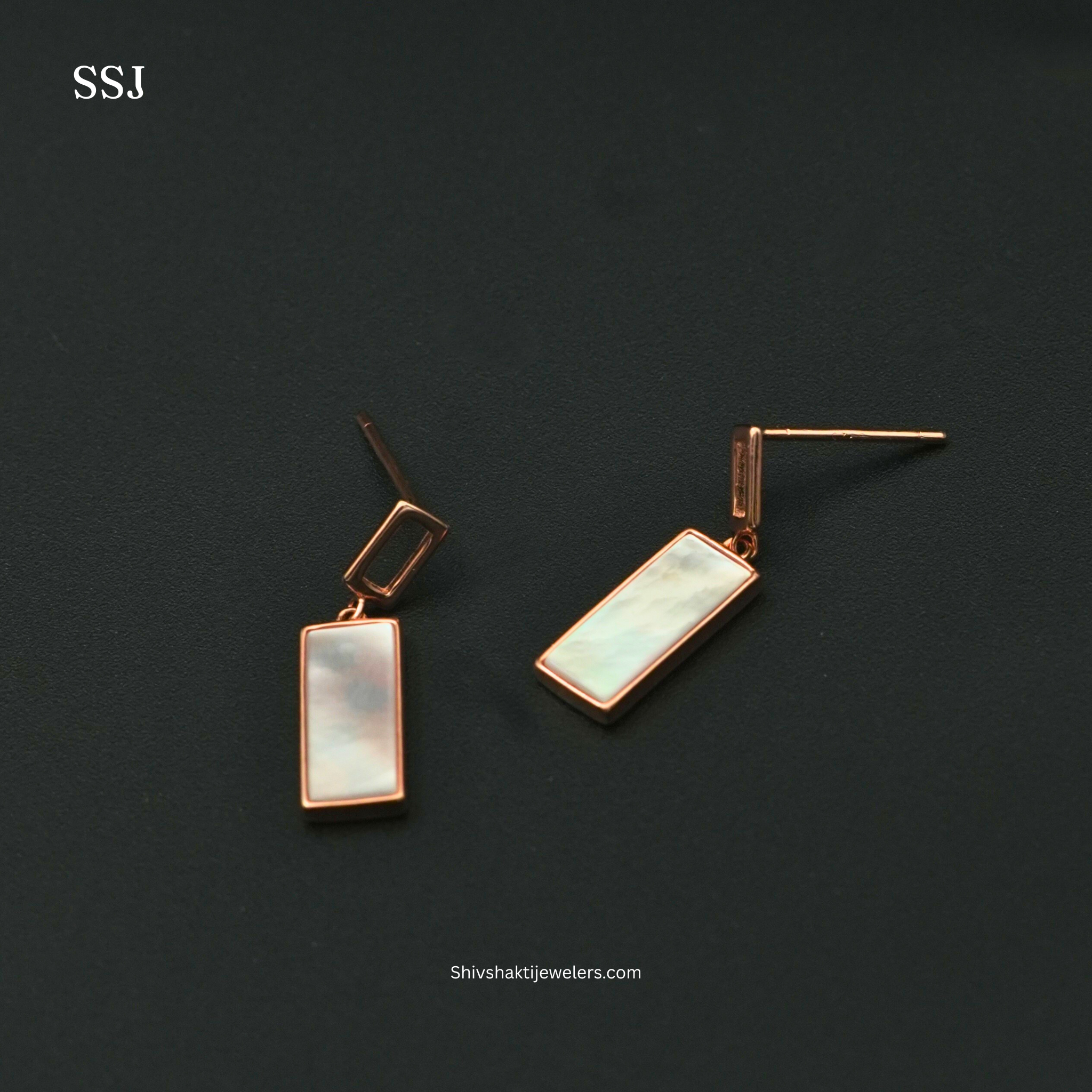 Pair of gold earrings with rectangular gemstones on a dark background